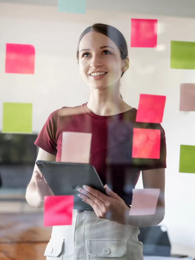 young-smiling-caucasian-businesswoman-mentor-leader-write-tasks-creative-ideas-sticky-post-it-notes-glass-wall